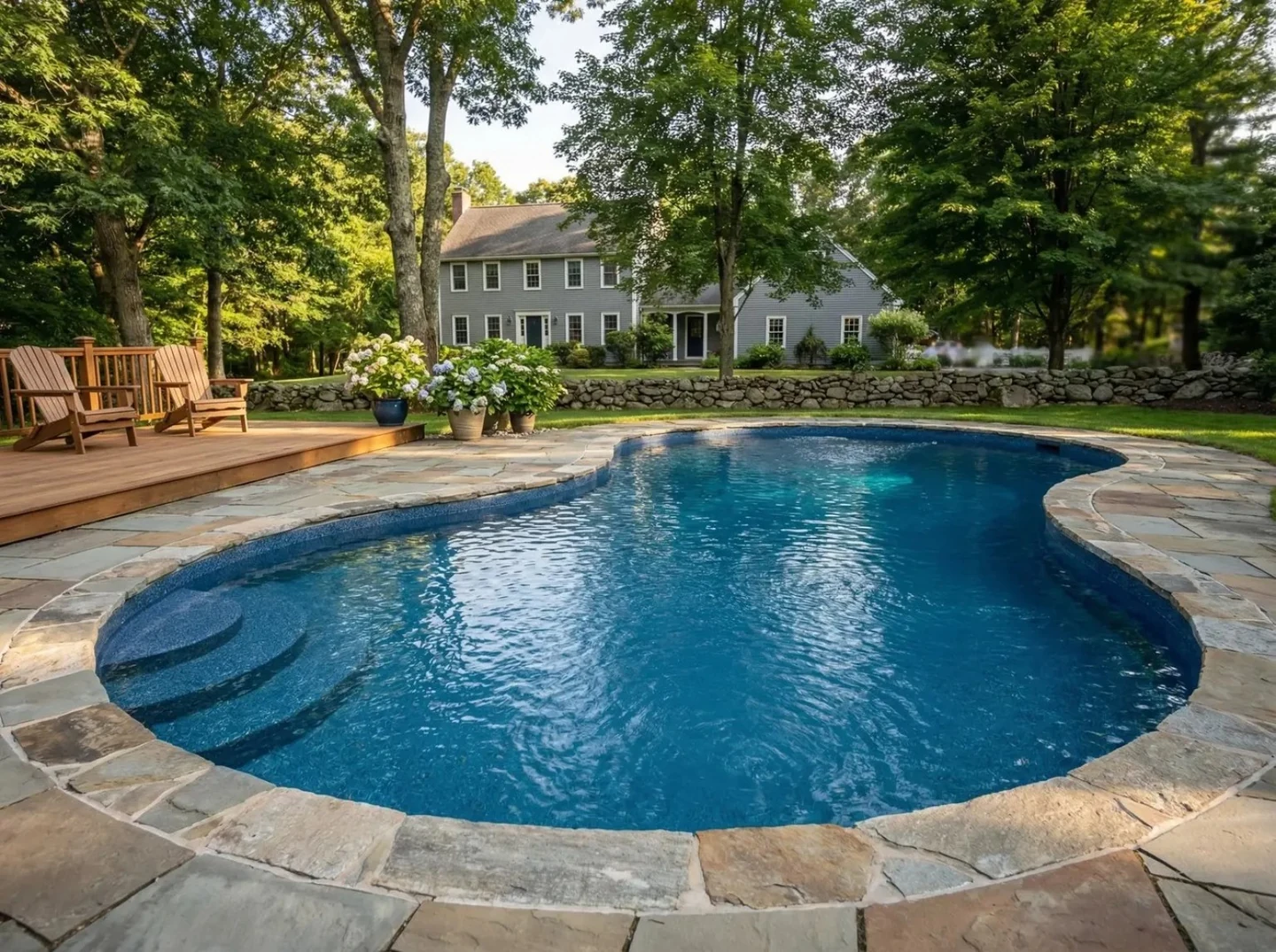 Backyard freeform pool with stone coping and steps by wooden deck