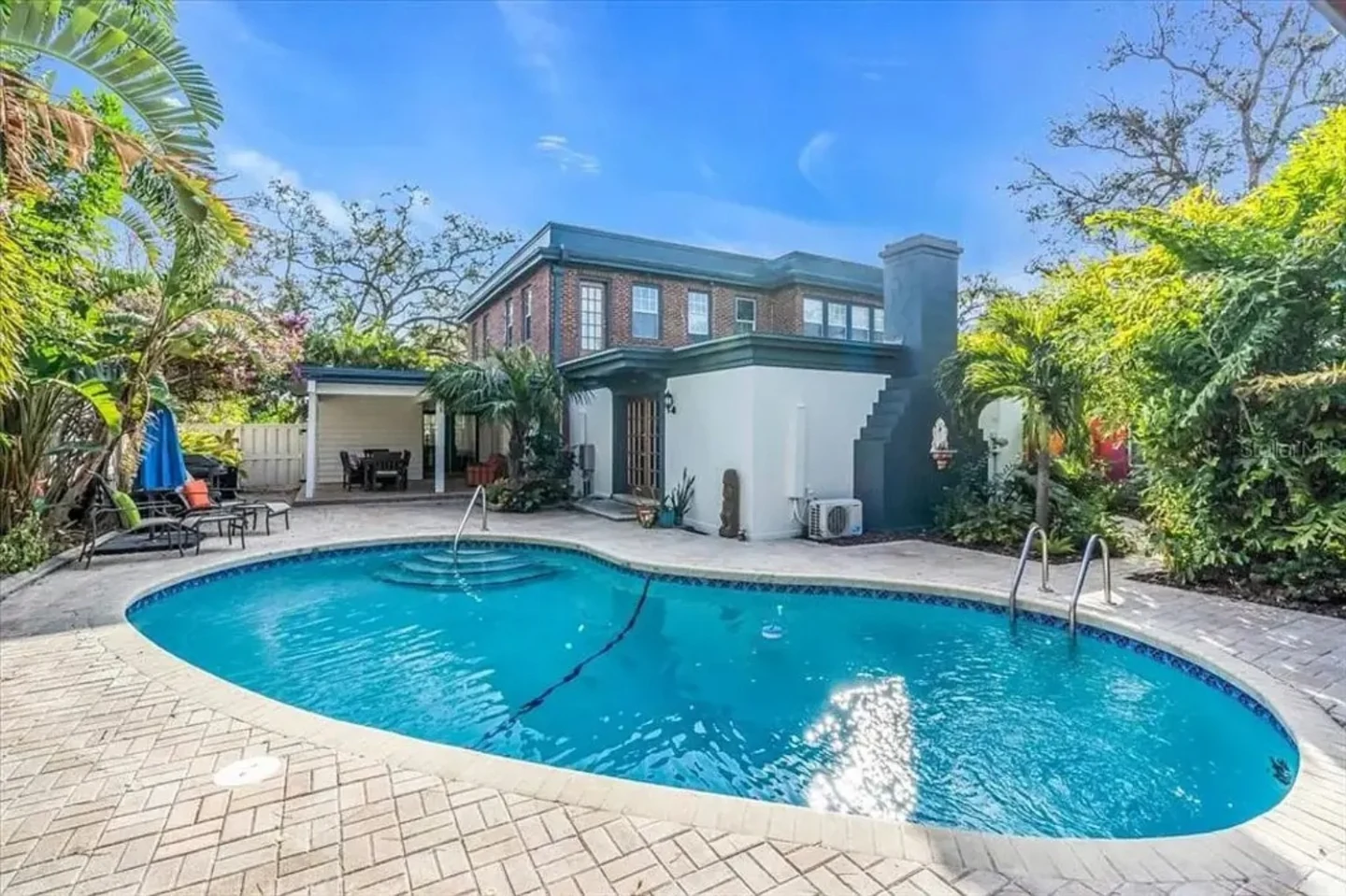 Oval residential pool with curved stairs, paver deck, tropical landscaping, and railing