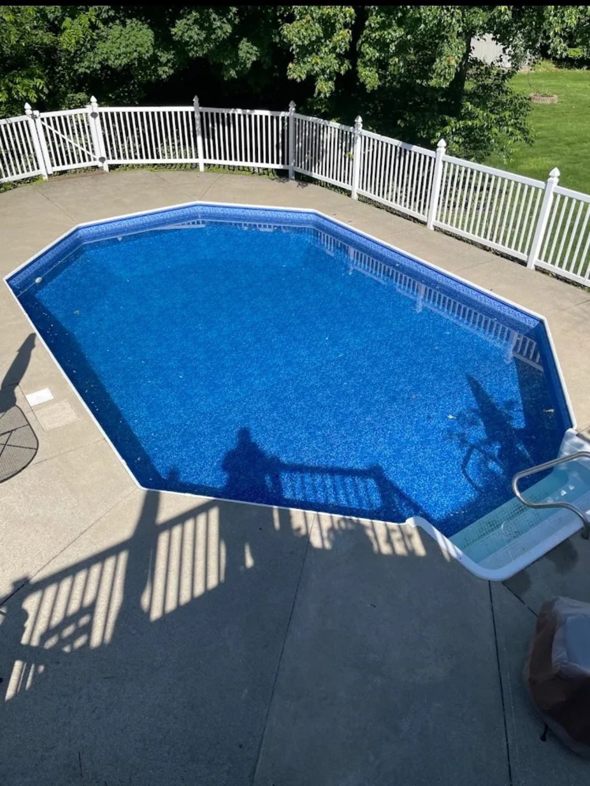 Octagonal blue-lined pool with white fence and concrete decking in daylight